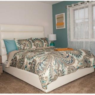 A stylish bedroom featuring a bed with patterned bedding and pillows, accented by a teal wall and natural light from a window with sheer curtains.