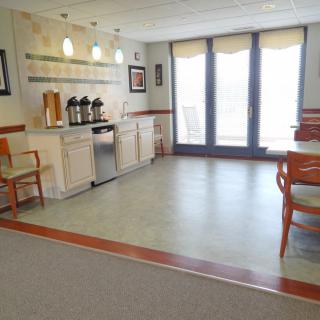 A cozy kitchen area with a coffee station, tables, and chairs by large windows.