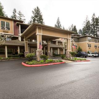 The image shows the front entrance of a large multi-story building with a covered driveway and surrounding trees.