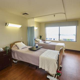 A hospital room with two patient beds and a large window offering natural light.