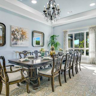 A beautifully decorated dining room featuring an elegant chandelier, a long dining table with chairs, and tasteful artwork on the walls.