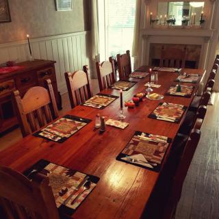A warmly lit dining room with a large wooden table set for a meal, featuring chairs and decorative placemats.