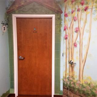 A wooden door with decorative mural art on the surrounding wall, featuring trees and greenery.