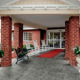 A welcoming entrance with red brick pillars, rocking chairs, and a red carpet leading to the doors.