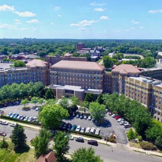 Aerial view of a large building complex surrounded by trees and a parking lot on a clear day.