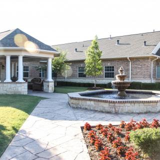 A beautifully landscaped courtyard featuring a fountain surrounded by flowers and a building in the background.