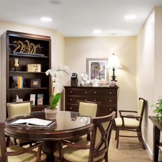 A well-furnished office space featuring a round table, chairs, a bookshelf, and decorative plants.