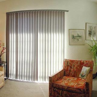 A cozy living room featuring vertical blinds, an armchair, artwork, and plants.