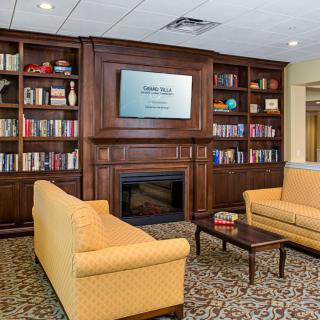 A cozy library room featuring wooden bookshelves, a television above the fireplace, and comfortable yellow couches.