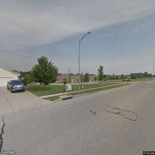 A suburban street view showing a residential neighborhood with houses, a car parked in a driveway, and a lamp post along the sidewalk.