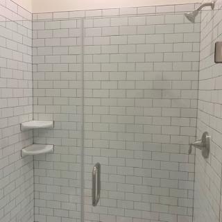 A modern bathroom shower with white subway tiles and a glass door.