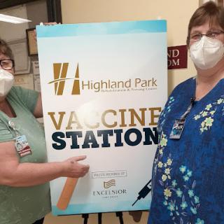 Two healthcare workers proudly display the Vaccine Station sign at Highland Park.