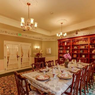 A beautifully decorated dining room with traditional wooden furniture, elegant table settings, chandeliers, and bookshelves lining the wall.