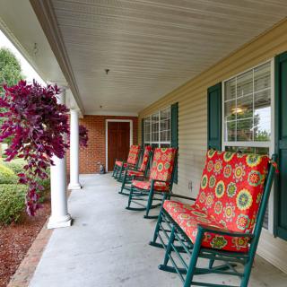 A cozy porch with colorful rocking chairs and lush greenery.