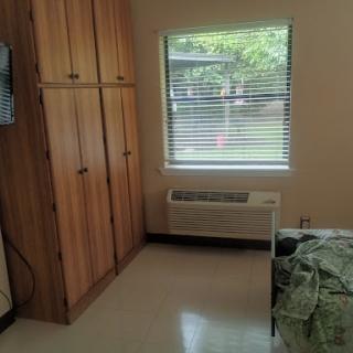 A simple and functional bedroom with wooden wardrobes, a window for natural light, and a bed.
