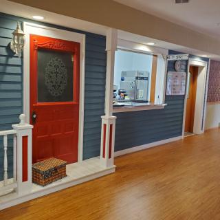 A well-lit indoor hallway with a red door and blue walls, featuring decorative lighting and wooden flooring.
