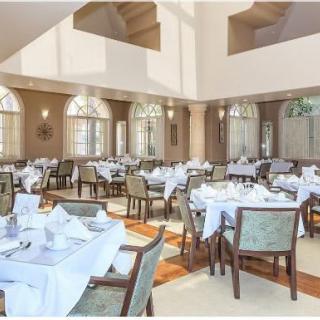 An elegant restaurant dining room with neatly arranged tables and chairs, featuring large windows and white tablecloths.