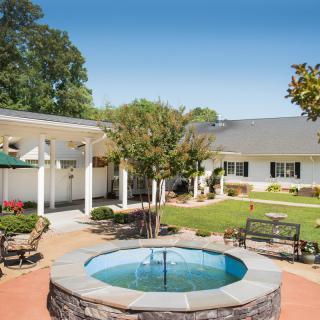 A serene courtyard featuring a fountain, surrounded by benches and lush landscaping.