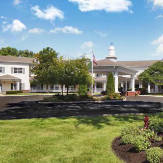 A scenic view of a large building surrounded by well-maintained lawns and trees under a partly cloudy sky.