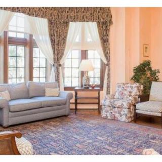 A cozy living room with a sofa, armchair, and large windows adorned with curtains.