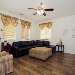 A cozy living room with a black sectional sofa and a large ottoman, featuring elegant curtains and a ceiling fan.