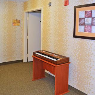 A hallway featuring an organ on a wooden stand with artwork on the wall.