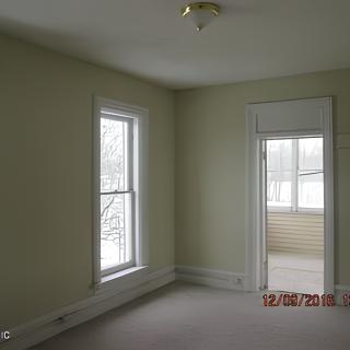 An empty room with large windows and beige walls, featuring a small light fixture on the ceiling.