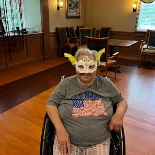 A joyful individual wearing a colorful mask and an American flag-themed shirt, seated in a wheelchair.