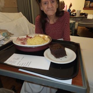 A patient in a hospital room enjoying a meal consisting of eggs and bacon, accompanied by a dessert.