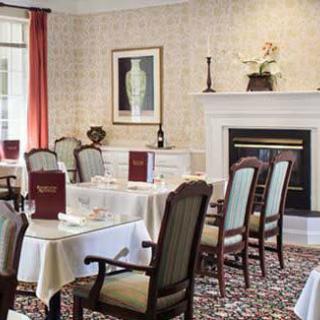 An elegant dining room with neatly arranged tables and chairs, featuring a fireplace and artwork on the wall.