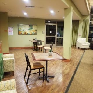 A cozy lobby area featuring tables and chairs, accented by green walls and warm lighting.