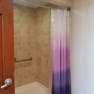 A bathroom with a tiled shower area featuring a purple gradient shower curtain and a grab bar.