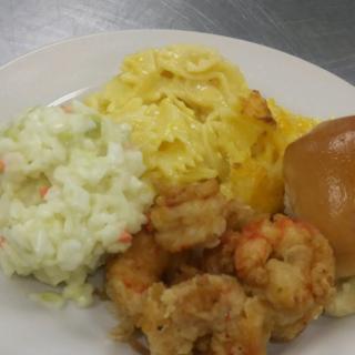 A plate of fried shrimp served with coleslaw, mac and cheese, and a bread roll.