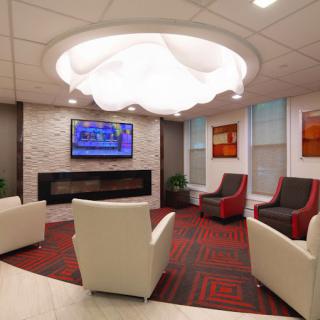 A modern lobby featuring comfortable seating, a stylish light fixture, and a wall-mounted television above a fireplace.
