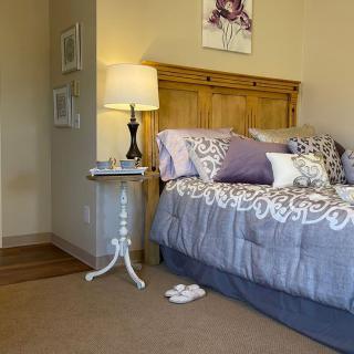 A cozy bedroom with a neatly made bed adorned with decorative pillows, a wooden headboard, and a small side table featuring a lamp.