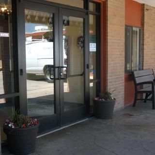 A building entrance with glass doors, flanked by planters and a bench.