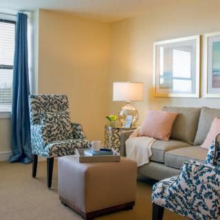 A cozy modern living room with a sofa, patterned armchairs, and a small coffee table, adorned with cushions and a lamp.