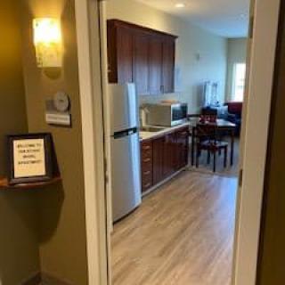 A view into a modern kitchen and dining area with wooden flooring, featuring a refrigerator and microwave.