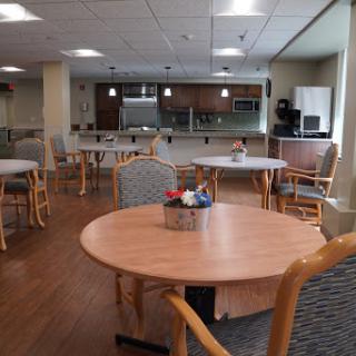 A spacious dining area featuring wooden tables and chairs, with a kitchenette in the background.