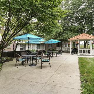 A serene outdoor patio with tables, chairs, and umbrellas next to a gazebo surrounded by trees.