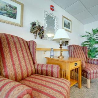 A cozy living room setup featuring striped armchairs, a wooden side table with a lamp, and decorative wall art.