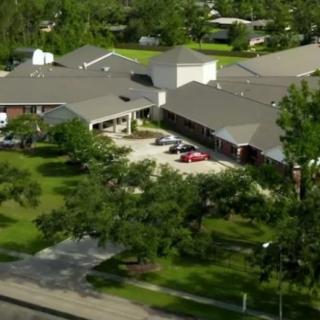 Aerial view of a building surrounded by trees and a parking lot in a residential area.