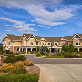 A large residential building surrounded by landscaped gardens under a blue sky with clouds.