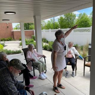 A group of seniors enjoying an outdoor activity on a patio, led by a person pointing at something in the distance.