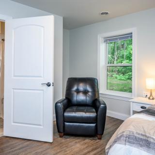 A cozy bedroom with a leather chair, bedside lamp, and open window.