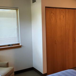 A minimalist bedroom with a wooden closet and window featuring closed blinds.
