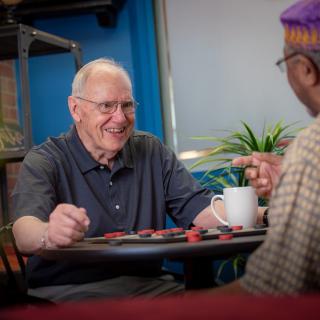Two elderly men enjoying a game and conversation in a cafe setting.