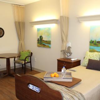 A cozy hospital room with a bed, a small table, and decorative paintings.