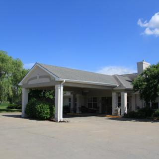 A building with a columned entrance and driveway, surrounded by trees under a clear blue sky.