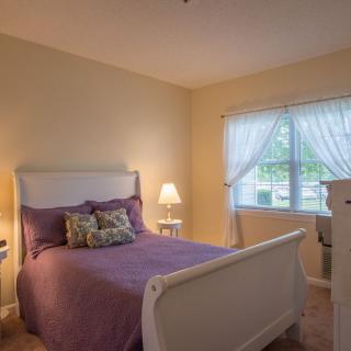 A cozy bedroom with a white bedframe, purple bedding, and two bedside lamps.